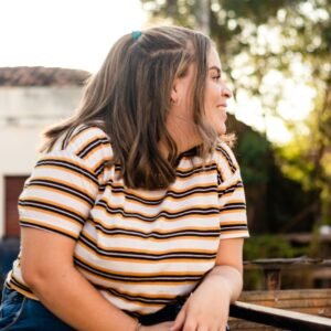 Casually posing woman with brown hair smiling, wearing a striped top, enjoying an outdoor setting.