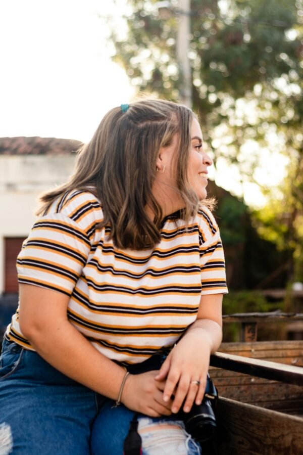 Casually posing woman with brown hair smiling, wearing a striped top, enjoying an outdoor setting.